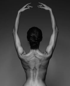 a woman with her back to the camera and hands behind her head, in black and white