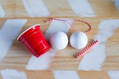 two white balls and a red cup sitting on top of a wooden table next to candy canes