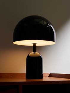 a black table lamp sitting on top of a wooden desk next to a white wall