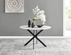 a white table with two vases on it in front of a gray wall and rug