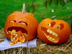 two pumpkins with faces carved into them sitting on hay in front of a fence