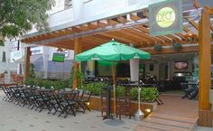 an outdoor dining area with tables, chairs and green umbrellas on the outside patio