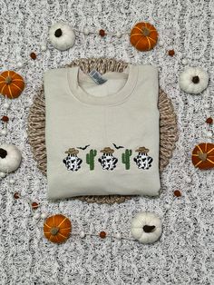 a sweater with three cows on it sitting next to pumpkins