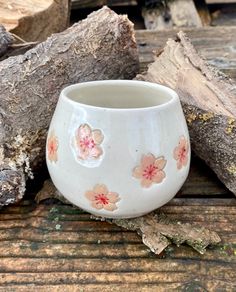 a white cup with pink flowers on it sitting next to some logs and tree trunks