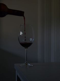 a person pours red wine into a glass in the dark, on a table