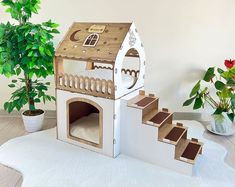 there is a cardboard house with stairs and a dog bed on the floor next to a potted plant