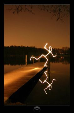 a light painting is shown on the water near a dock with trees in the background