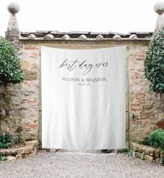 an outdoor wedding ceremony with a white sign and greenery on the side of the building