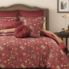 a bed with red comforter and pillows on top of it in front of a lamp