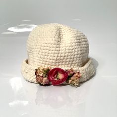 a white crocheted hat with flowers on the brim and side, sitting on a table