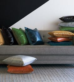 the pillows are stacked on top of each other in front of a gray couch with multicolored cushions