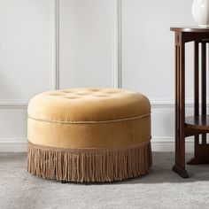 a round ottoman sitting next to a table with a chair in front of it and a small stool on the other side