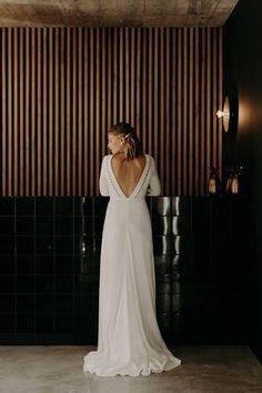 a woman standing in front of a black wall wearing a white dress and holding her back to the camera