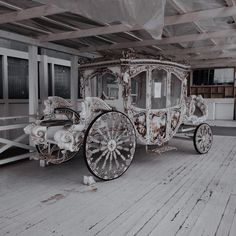 a white horse drawn carriage sitting on top of a wooden floor next to a building