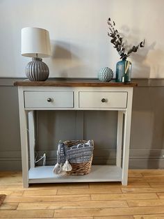 a white table with two drawers and a basket on it next to a light blue lamp