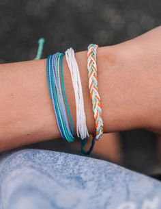 a person wearing three different colored bracelets on their arm and one with an orange, white, and blue cord