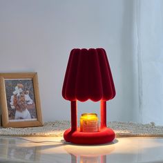 a red lamp sitting on top of a white table next to a framed photo and a candle