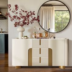 a white and gold sideboard in a room with a round mirror on the wall