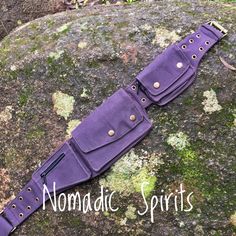 a purple leather watch strap with gold studs on it sitting on top of a mossy rock