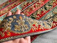 a hand holding an old piece of cloth with gold and red trimmings on it