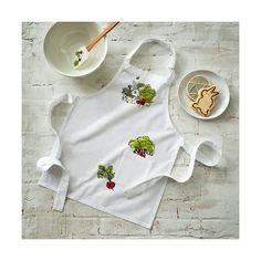 a white apron with broccoli and radishes on it next to a bowl