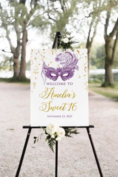 a welcome sign with a mask on it in front of some trees and flowers at an outdoor wedding