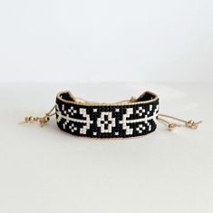 a black and white beaded bracelet on a white surface with two gold - plated beads