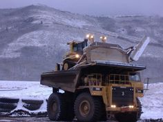 a large dump truck driving down a snow covered road in front of a snowy mountain