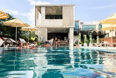 people are relaxing in the swimming pool near an apartment building with yellow and white umbrellas