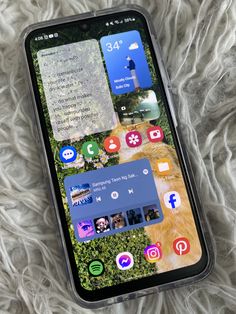 an iphone with several different apps on the screen sitting on top of a white blanket