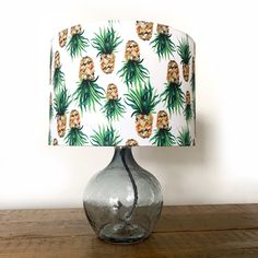 a table lamp with a pineapple print shade on top of it, sitting on a wooden surface