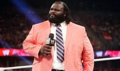 a man in a suit and tie holding a microphone while standing on a wrestling ring