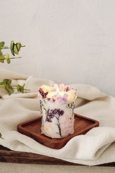 a lit candle sitting on top of a wooden tray next to some flowers and leaves