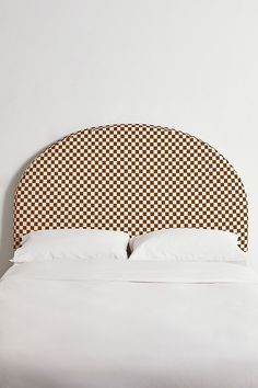 an upholstered headboard on a bed with white sheets and brown checkered pillows