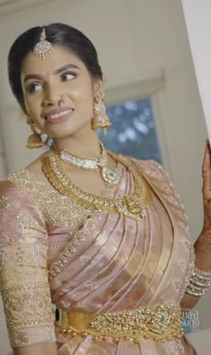 a woman in a pink and gold sari holding her hand up to the side