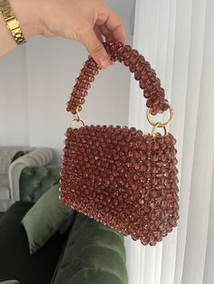 a hand holding a brown beaded purse in front of a green velvet couch with white curtains