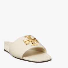 A single-band slide is made of soft leather and distinguished by our sculptural Eleanor hardware — redesigned with scaled-down dimension.Crafted in partnership with a Leather Working Group-certified tannery, supporting high standards in leather manufacturing and chemical management. White Tory Burch Sandals, Fashion Sandals Flat, Tory Burch Eleanor, Semi Annual Sale, Tory Burch Sandals, High Standards, Footwear Design Women, Designer Sandals, Sandal Fashion