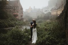 a bride and groom standing on a path in front of a river surrounded by tall buildings