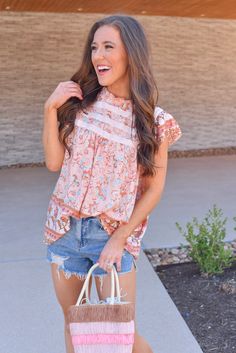 Level up your spring tops with this fun floral top in peachy orange! Pair it with denim shorts or white denim for an eye catching spring look. Floral high neck top Flowy fit Flutter sleeves Gorgeous pattern throughout Button closure up top in back Full coverage Runs true to size Also available in Sky Blue Piper is 5'3, wears a size 2 and is wearing a Small! Spring Floral Print Tops With Flutter Sleeve, Casual Flutter Sleeve Top For Spring, Orange Short Sleeve Tops For Spring, Casual Flutter Sleeve Blouse For Spring, Casual Spring Blouse With Flutter Sleeves, Peach Floral Print Summer Blouse, Summer Tops With Flutter Sleeves, Spring Summer Tops With Flutter Sleeves, Trendy Floral Print Top With Flutter Sleeves