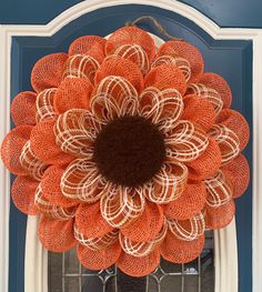 an orange and white mesh wreath hanging on the front door with a brown center piece