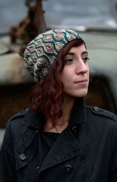 a woman with red hair wearing a knitted hat in front of an old car