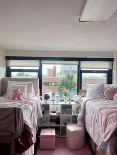 two beds in a bedroom with pink carpeting and large windows overlooking the city outside