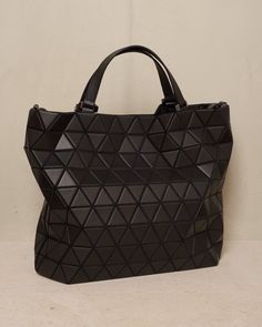 Easy large tote bag by Bao Bao Issey Miyake in black. Large carry-all tote with detachable shoulder strap in cowhide leather. Matte triangular tiles tessellate the exterior surface with a matte leather-like finish. Large internal capacity with secure pockets and nylon lining. Synthetic Leather, Polyester, Cowhide Leather.Made in Japan. Bao Bao Issey Miyake, Bao Bao, Large Tote Bag, Issey Miyake, Black Tote Bag, Large Tote, Synthetic Leather, Cowhide Leather, Made In Japan