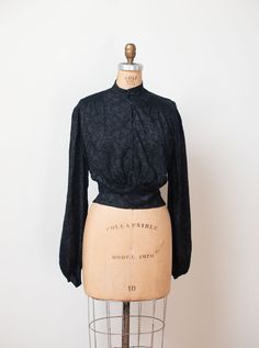 "Antique embroidered black blouse c. 1900 with gathering at the shoulders, long bishop sleeves with self fabric buttons at the cuffs and self fabric ties at the back. Metal snaps at the front. Feels like silk or a silk blend. - Size Small / Medium / Large - Blousy style tie to fit. Displayed unclipped on dress form with 35\" bust. Shoulder: 16\" Bust: 44\" - 46\" Waist: 42\" Length: 18.5\" Sleeve Length: 26\" Condition: Excellent! - One small hole as pictured. Only seen when held up to light. - Classic Black Blouse With Blouson Sleeves, Fitted Blouse With Smocked Cuffs And Bishop Sleeves, Black Long Sleeve Blouse With Lace Cuffs, Formal Fitted Blouse With Gathered Sleeves, Formal Long Sleeve Blouse With Gathered Sleeves, Formal Black Tops With Lace Cuffs, Black Lantern Sleeve Blouse For Formal Occasions, Vintage Fitted Blouse With Gathered Sleeves, Vintage Bishop Sleeve Formal Blouse