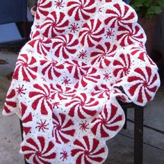 a red and white crocheted afghan with candy canes on it, sitting in front of a potted plant