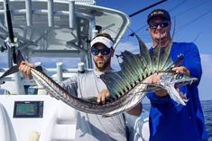 two men on a boat holding up some kind of fish that they are holding in their hands