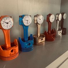 there are five different clocks on the wall together in this row, one is orange and one is blue