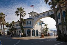 the front entrance to a hotel with palm trees and people walking around it on a sunny day