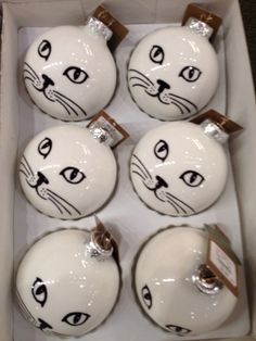 six white ceramic ornaments with black cats painted on them in a cardboard box, each decorated as a cat's head