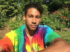 a young man in a tie dye shirt is posing for a photo with his arms crossed